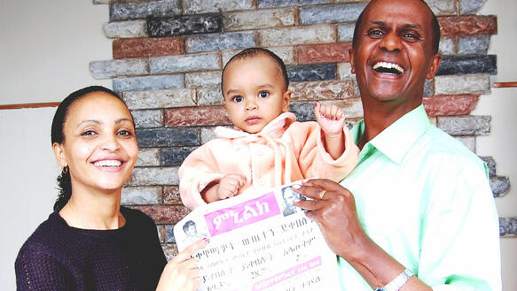 Eine Frau und ein Mann halten ein Kleinkind und eine Zeitung in ihrer Mitte