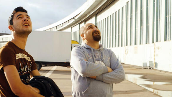 Zwei Männer stehen vor dem Flughafen Tempelhof und blicken in den Himmel