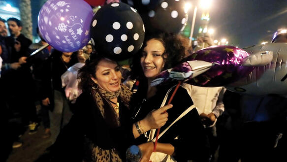 Zwei Frauen umarmen sich auf der Straße in der Nacht und lachen, umgeben von Luftballons