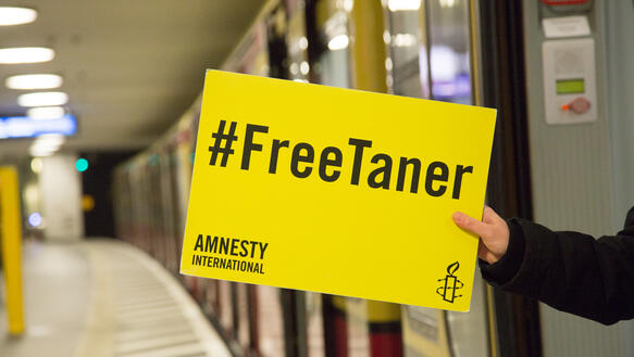 Ein gelbes Schild, auf dem #FreeTaner steht, wird aus der S-Bahn gehalten