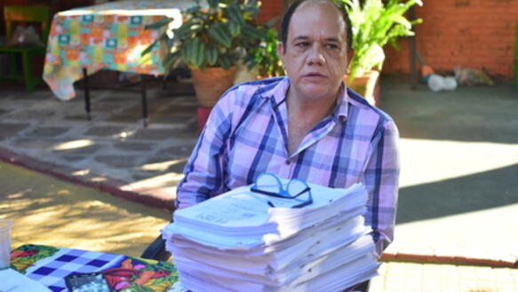Mann in lila Hemd sitzt vor einem Stapel Papier