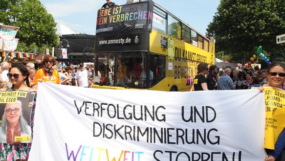 Ein Transparent gegen Diskriminierung, dahinter Menschen und ein gelber Bus