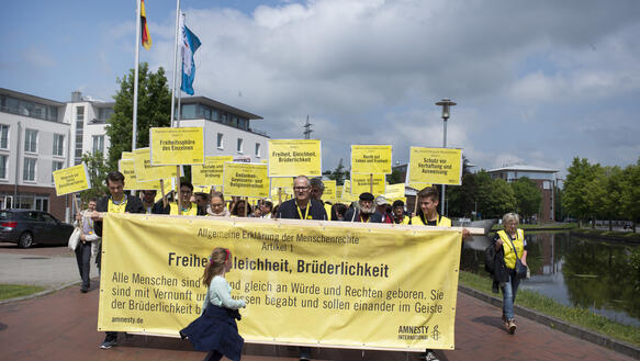 Amnesty-Mitglieder gehen mit Transparenten und Bannern, auf denen die Artikel der Allgemeinen Erklärung der Menschenrechte abgebildet sind, auf einer Strasse in der Stadt Papenburg