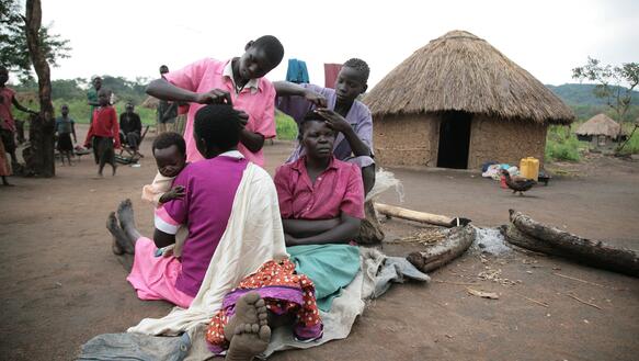 Frauen und Kinder sitzen vor ihrer Hütte auf dem Boden