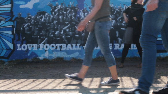Menschen laufen vor einem Graffito mit dem Schriftzug Love Football, Hate Racism