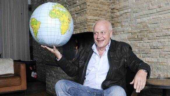 Ein Mann sitzt in einem Sessel und hält in der rechten Hand einen Globus