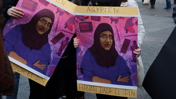 Zwei junge Frauen halten Plakate mit einer Grafik von Hanan Badr el-Din in der Hand