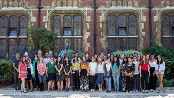 Eine Gruppe von etwa 40 jungen Männern und Frauen steht vor den Mauern der Cambridge Universität