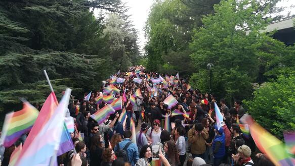Viele Menschen auf einem Weg zwischen Bäumen mit Regenbogenflaggen