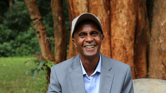 Portrait von Eskinder Nega, der eine Kappe und ein Jacket trägt, im Hintergund steht ein großer Baum