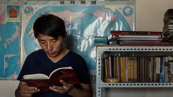 Ein junger Mann steht neben einem Bücherregal und liest in einem Buch
