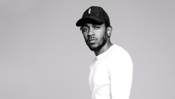 Der Rapper Kendrick Lamar mit schwarzer Cappy und weißem Oberteil vor grauem Hintergrund