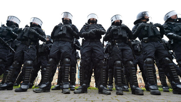Eine Gruppe von Polizeikräften mit Helmen und Schienbeinprotektoren steht in einer Reihe