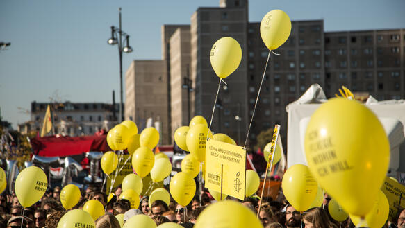 Viele gelbe Amnesty-Luftballons fliegen über einer Menschenmenge
