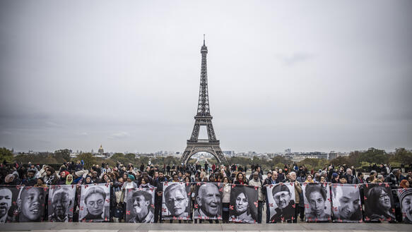 Menschen stehen auf einem Platz vor dem Eiffeltum und halten Schilder mit Porträts von Menschenrechtsverteidigerinnen und -verteidigern