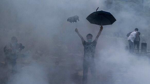 Ein Mann hält zwei Regenschirme hoch, um ihn sind Rauchschwaden