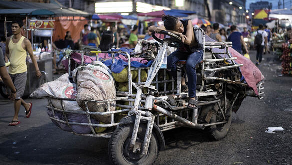Eine Frau hat den Kopf auf das Lenkrad ihres Lastenfahrrads gelegt, das auf einem belebten Markt steht