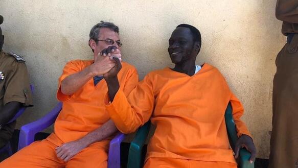Zwei Männer in orangenen Häftlingsoveralls geben sich die Hand und lächeln