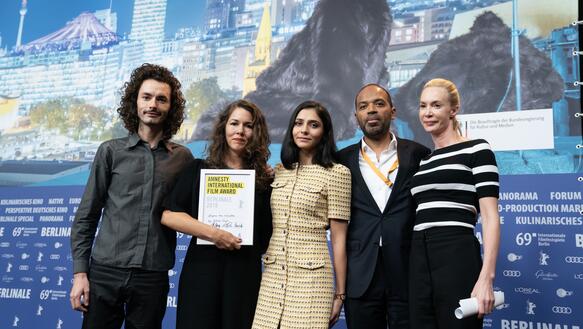 Drei Frauen und zwei Männer stehen nebeneinander, eine der Frauen hält eine Urkunde in der Hand, auf der steht: "Amnesty International Film Award Berlinale 2019"