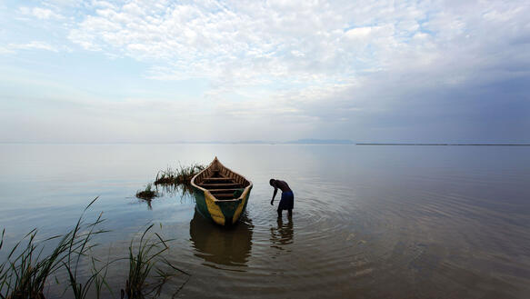 Eine Boot auf einem See, daneben ein Mann im wasser in gebückter Haltung.