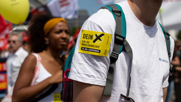 Viele Personen demonstrieren, eine der Personen hat sich am Oberarm den Amnesty-Aufkleber "Dein X für die Menschenrechte" auf das T-Shirt geklebt