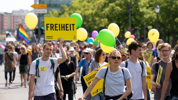 Viele Menschen demonstrieren mit Schildern, Lufballons und Fahnen auf einer Straße