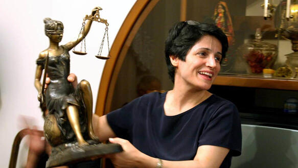 Foto einer lächelnden Frau, die nach rechts schaut und die eine Justitia-Skulptur in den Händen hält