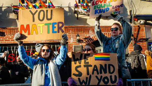 Im Vordergrund stehen drei Frauen mit Protestschildern vor dem Stonewall Inn in New York