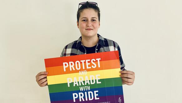 Vitalina Koval schaut frontal in die Kamera und hält ein Schild in Regenbogenfarben vor sich. Auf dem Schild steht "Protest and Parada with Pride" geschrieben.