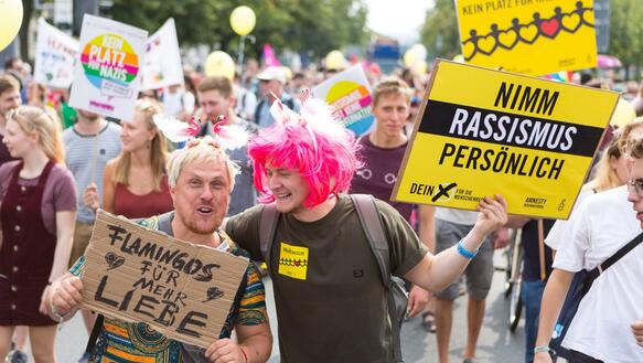 Menschen mit Plakaten demonstrieren "Nimm Rassismus persönlich, "Flamingos für die Liebe"