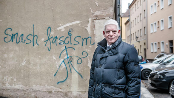Ein Mann vor einer Hauswand, die mit einem Graffiti verschmiert ist