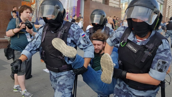 Polizisten tragen einen Mann an Händen und Füßen