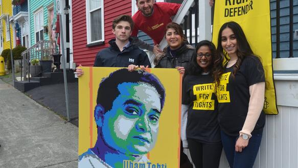 5 Jugendliche halten ein Plakat mit dem Bild von Ilham Tohti und ein Amnesty-Transparent in die Kamera.