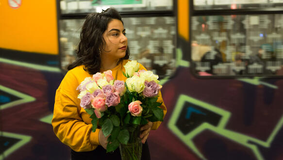 Junge Frau mit ein Strauß Rosen steht vor einer einfahrenden U-Bahn.