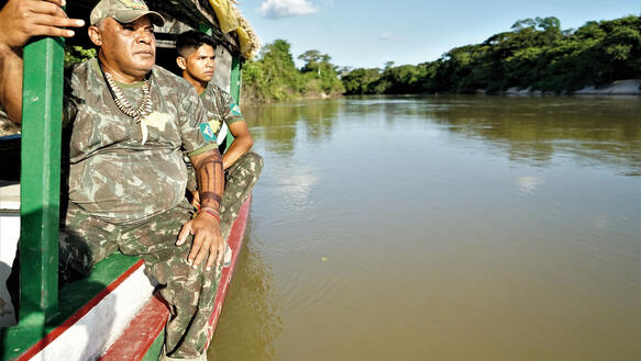 Zwei Männer in Militäruniform sitzen auf einem Boot und halten Ausschau.