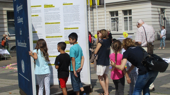 Kinder schauen sich die Allgemeine Erklärung der Menschenrechte als XXL Aufsteller an. 