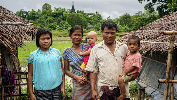 Eine Familie steht zwischen zwei Bambushütten in einer Waldsiedlung in Myanmar