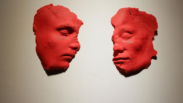 Zwei rote Gipsadrücke von zwei Gesichtern liegen auf einer weißen Fläche.