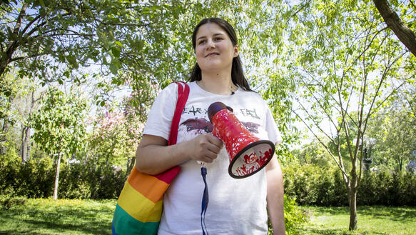 Frau mit Megaphon und Tasche in Regenbogenfarben steht an einem sonnigen Tag in einem Park