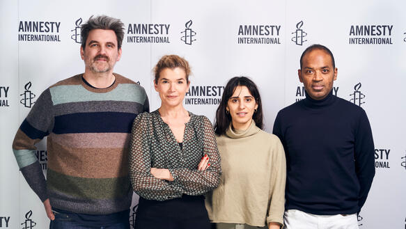 Zwei Männer und zwei Frauen stehen vor einer weißen Wand mit Amnesty-Logos