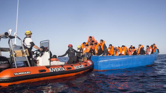 Rettungsboot nähert sich Geflüchteten, die Rettungswesten tragen