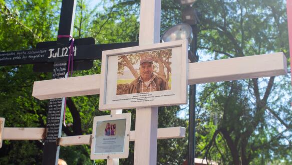 Ein weißes Holzkreuz im Vordergrund darauf das Porträt von Julian Carrillo