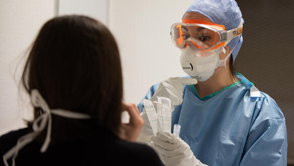 Frau mit Atemschutzmaske und Schutzbrille behandelt eine Patientin in einem Krankenhaus