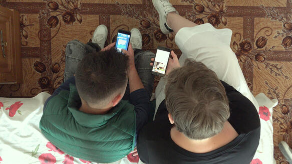 Zwei Männer sitzen eng zusammen und betrachten die Handys in ihren Händen.