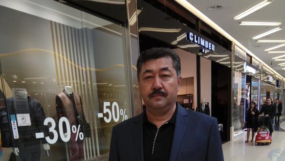 Ein Mann im grauen Anzug steht in einer Einkaufspassage und blickt ernst in die Kamera.