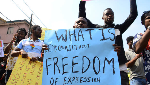 Menschen mit Protestplakaten mit der Aufschrift "Was ist Demokratie ohne Meinungsfreiheit?"