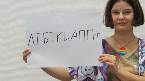 Eine junge Frau hält einen Zettel mit russischer Schrift in die Kamera.