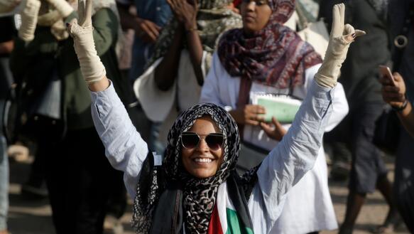 Frau mit Schaal und Sonnenbrille zeigt das Victory-Zeichen bei einer Demonstration