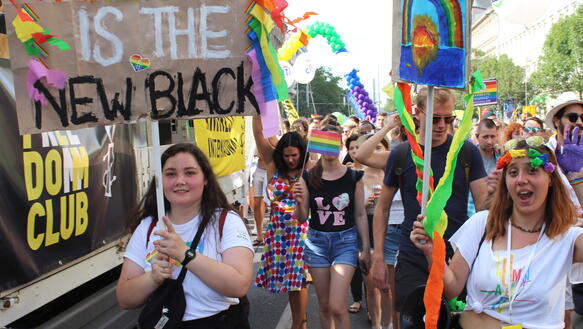Demonstration im Sommer, viele junge Menschen, mit Plakaten, Regenbogen-Motiven und Flaggen