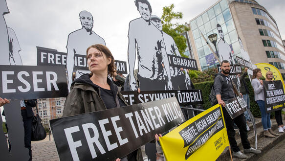 Eine junge Frau hält ein Schild in den Händen, dass die Freilassung des türkischen Rechtsanwalts und Menschrenrechtsverteidgers Taner Kılıç fordert. Neben ihr stehen weitere Aktivisten.